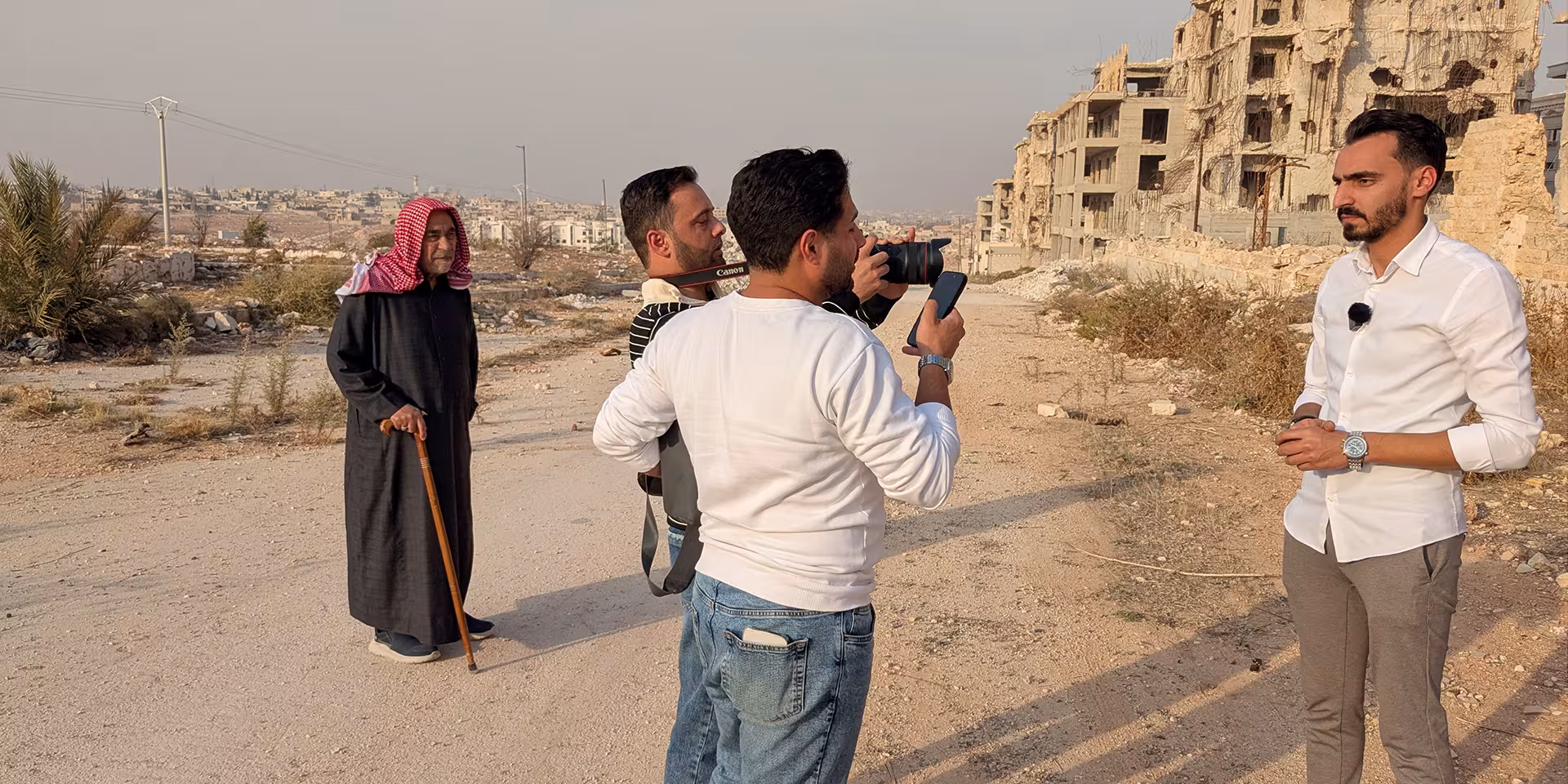 Ein Kamerateam filmt einen Mann vor stark zerstörten Gebäuden; ein älterer Mann steht daneben.