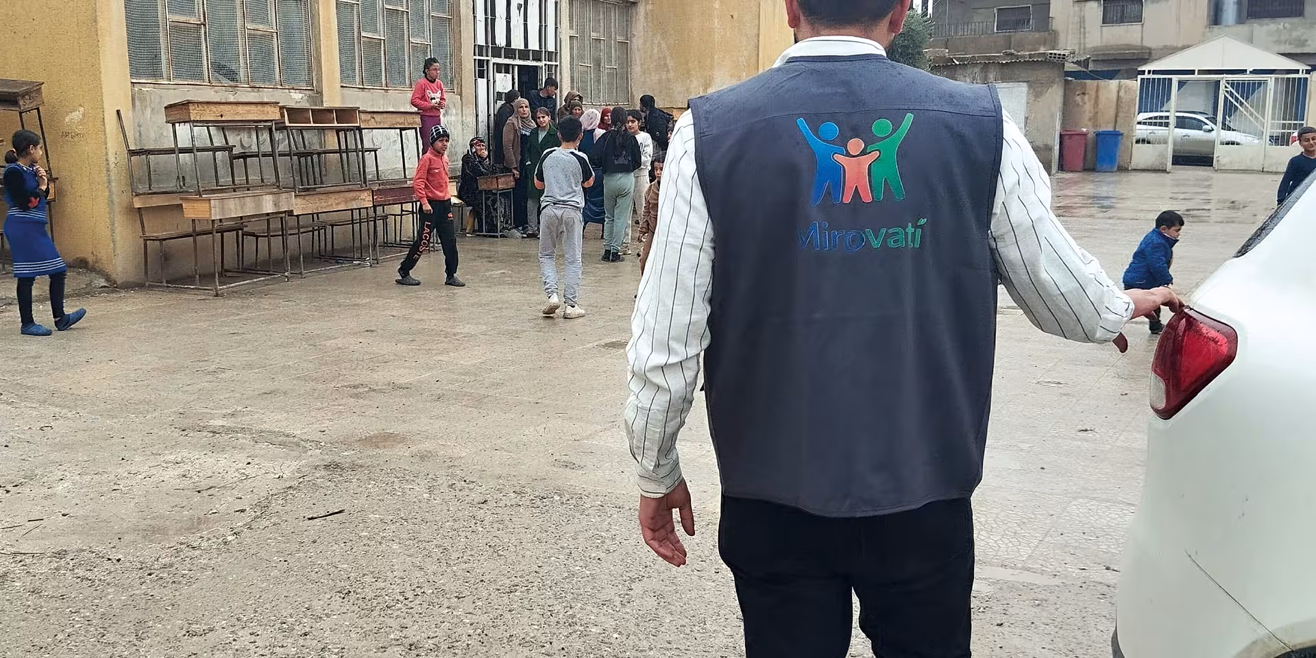 Ein Mitarbeiter einer Hilfsorganisation betritt einen Schulhof, auf dem Kinder und Jugendliche stehen.