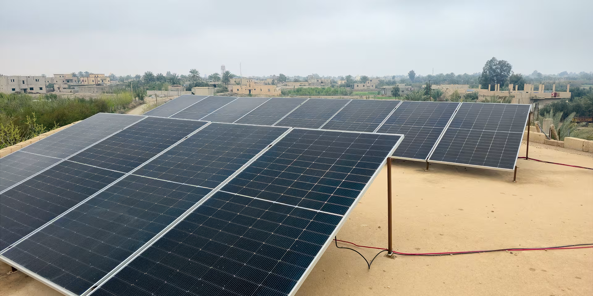 Große Solarmodule stehen auf einem Flachdach, im Hintergrund liegt eine ländliche Siedlung.