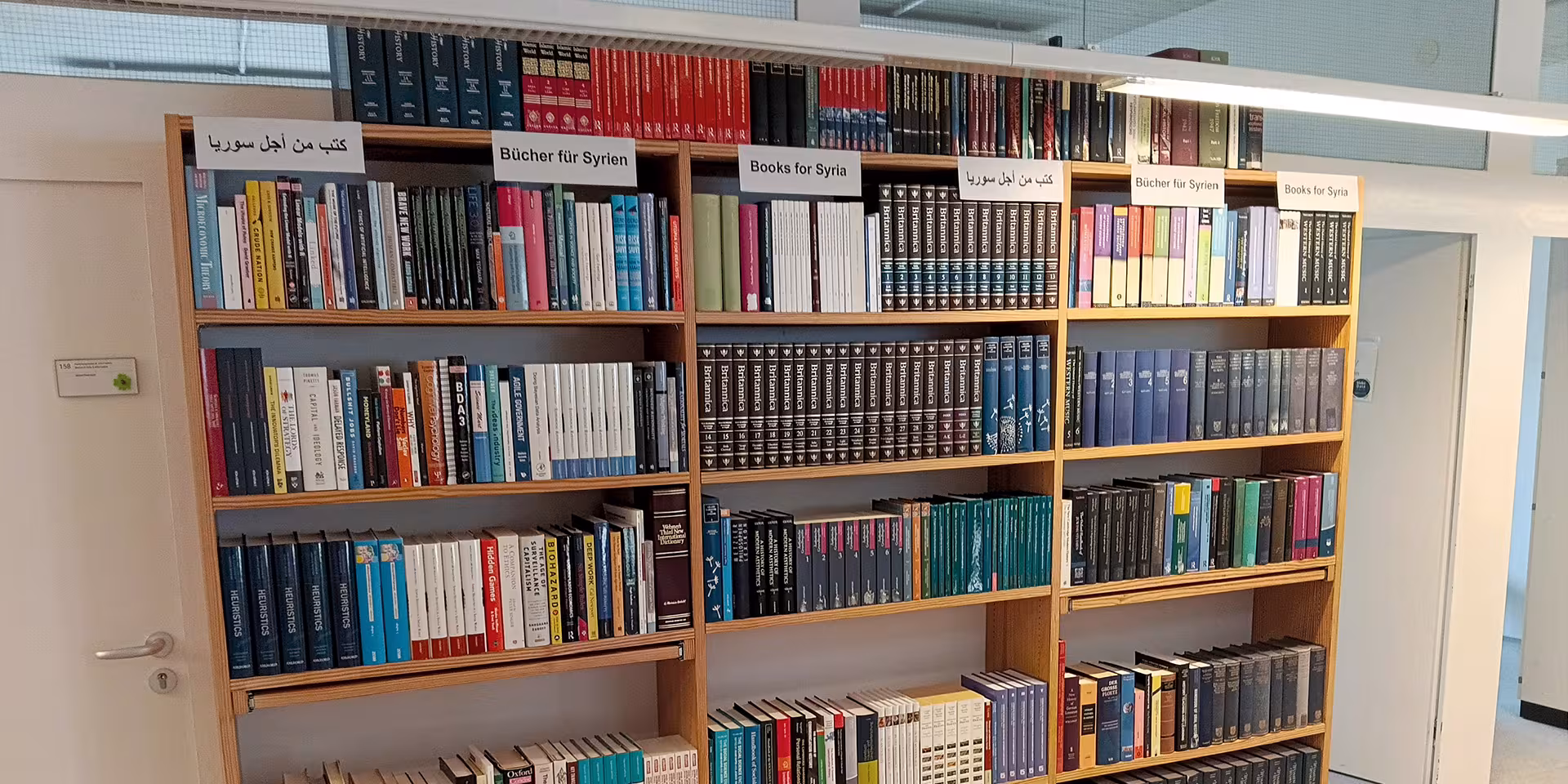 Bücherregale mit deutsch-, englisch- und arabischsprachigen Schildern für die Initiative „Bücher für Syrien“.